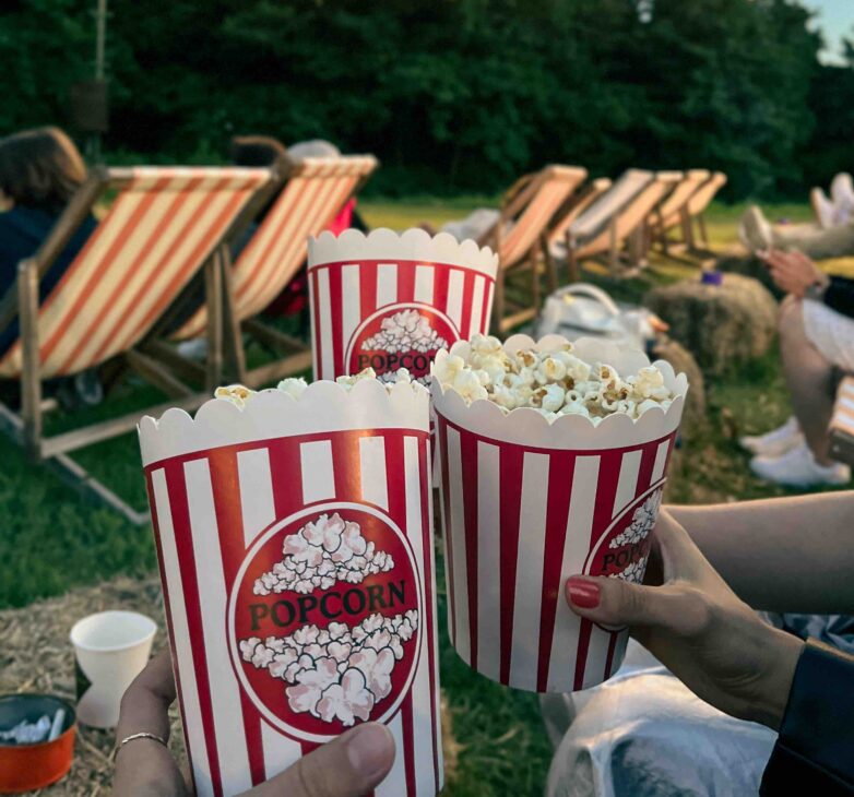 Friends holding out their popcorn ready to watch a film outdoors